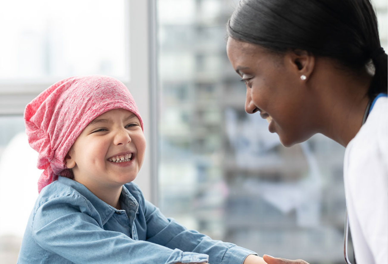 A doctor with a patient who is a child. The patient is smiling and wears a blue top and a red head scarf.